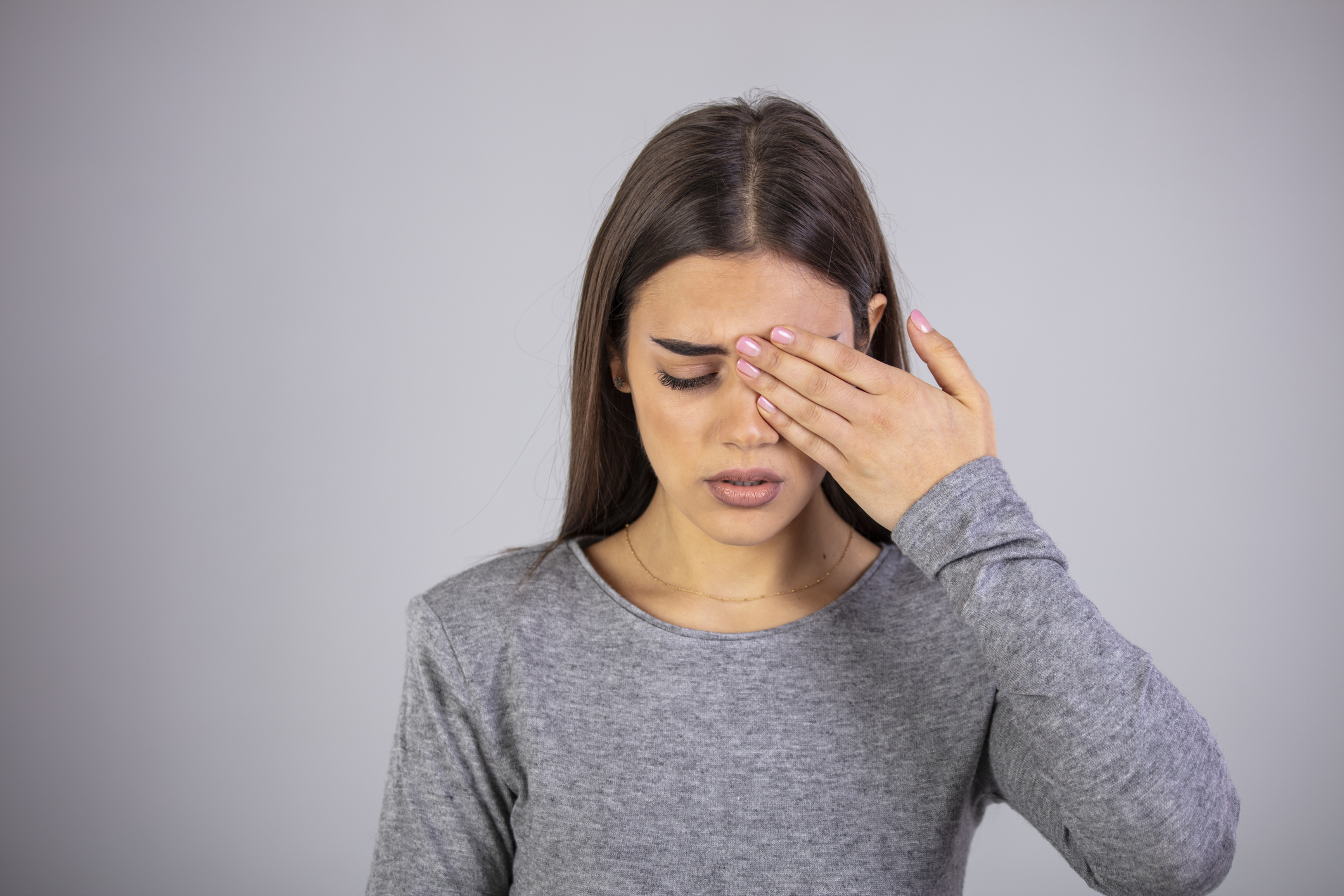 Young woman has pain in the eye. Young woman with of eye pain on a gray background. Woman is suffering of eye pain. Woman suffering from strong eye pain. Studio shot