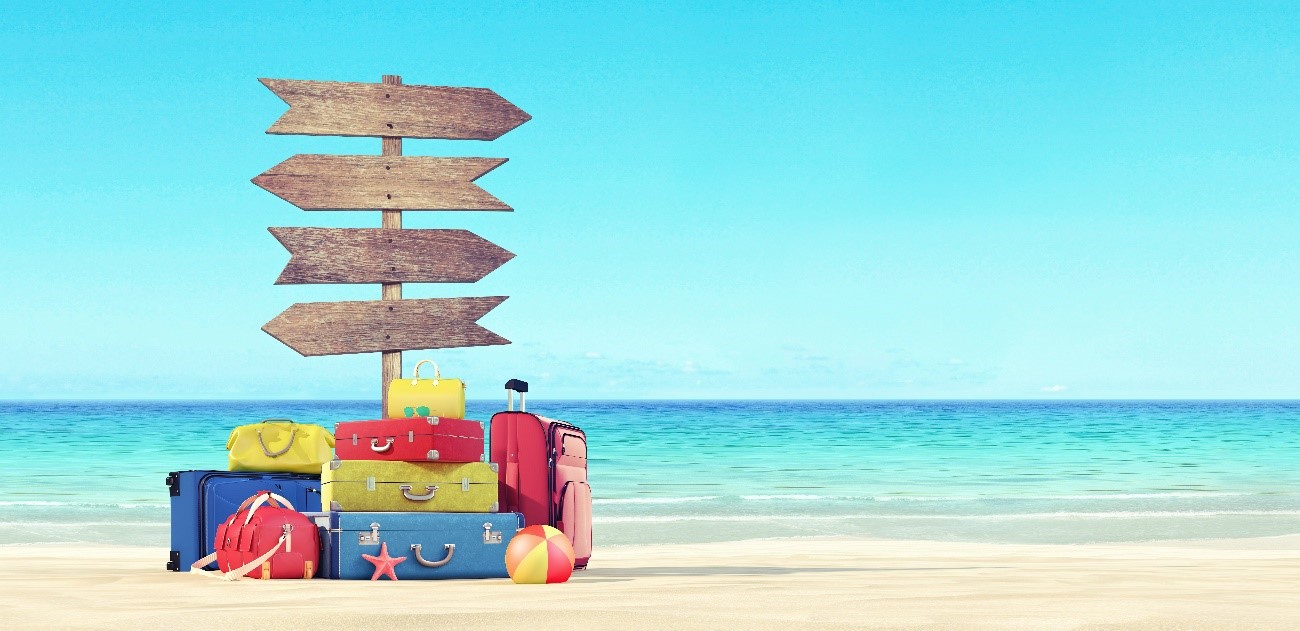 Imagen de una cartel, maletas y una playa por detrás. Simboliza las vacaciones de verano.