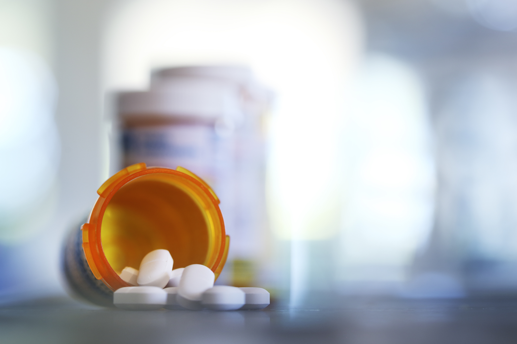 Pills pour out of a prescription medication bottle onto a kitchen counter.  Several other pill bottles stand out of focus in the background. (Pills pour out of a prescription medication bottle onto a kitchen counter.  Several other pill bottles stand