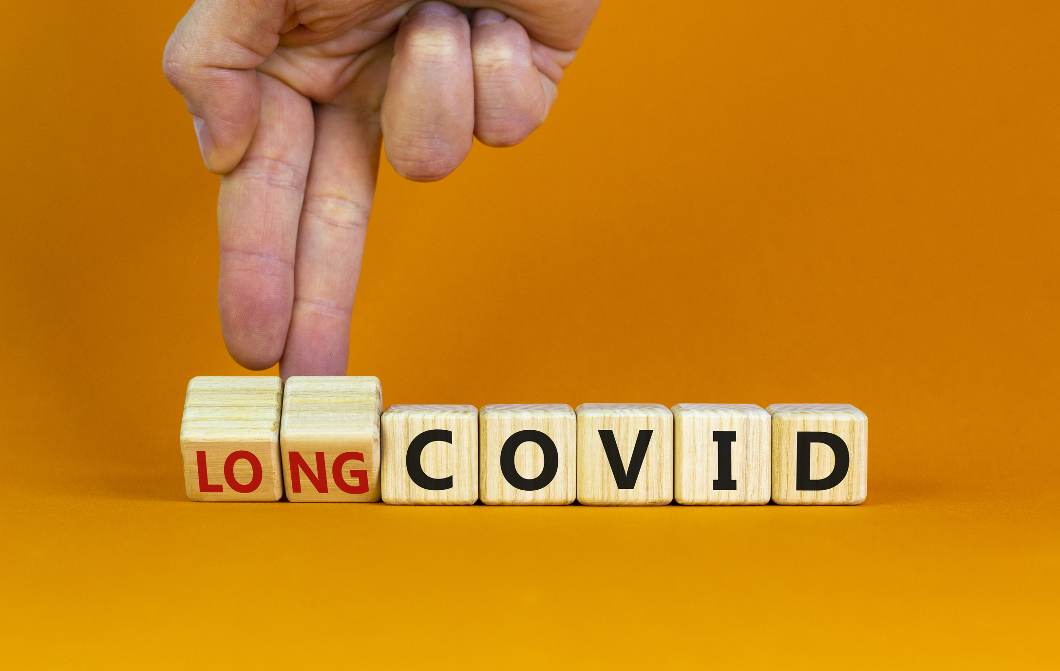 Long covid symbol. Doctor turnes wooden cubes and changes words 'covid' to 'long covid'. Beautiful orange background, copy space. Medical, covid-19 pandemic long covid concept. (Long covid symbol. Doctor turnes wooden cubes and changes words 'covid' t