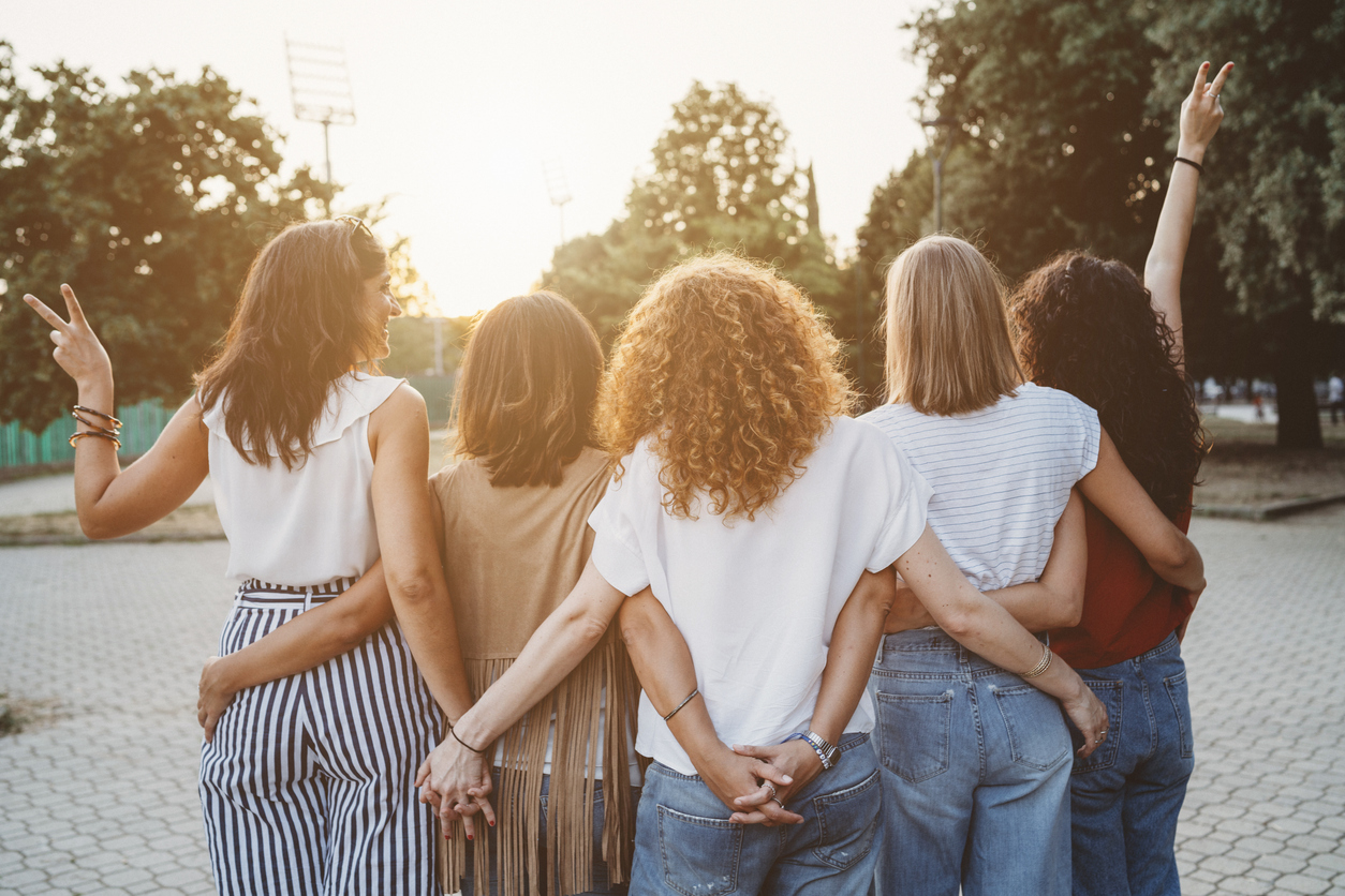 Group of women friends holding hands together against sunset