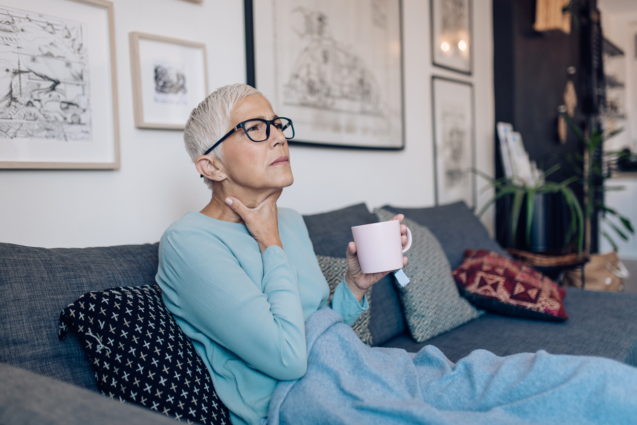 Senior woman having a flu, lying on the sofa and drinking tea.