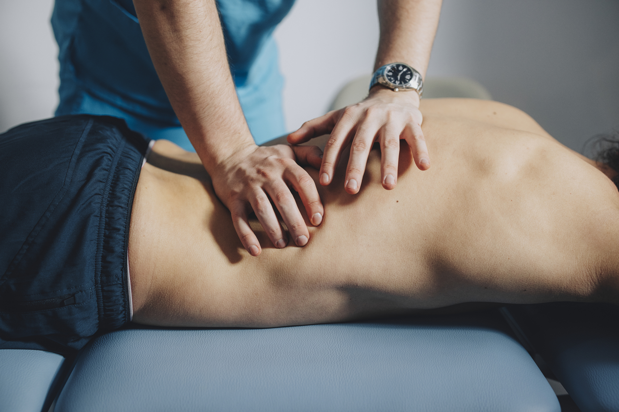 Physical therapist is using his hands to massage the lower back of a male patient lying on his stomach.