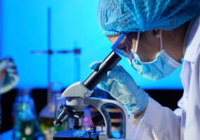 Profile view of concentrated Asian microbiologist examining sample with help of modern microscope while wrapped up in work at dim laboratory